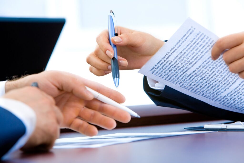 Hands exchanging a document and pens during a business meeting, illustrating legal discussions related to business litigation and contract agreements.