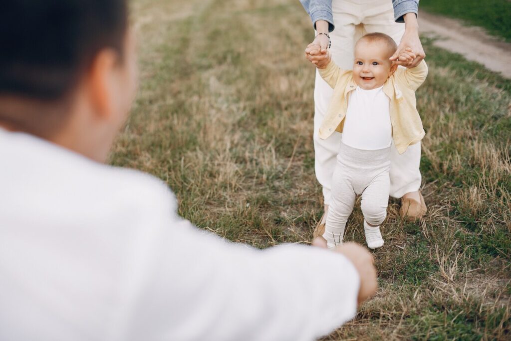 Child being held by an adult, smiling and taking steps on grassy field, symbolizing the joy of adoption and family bonding.