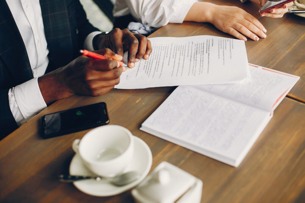 Hands of a person signing legal documents with a red pen, accompanied by a notebook and a smartphone, in a professional setting related to civil litigation and legal services.