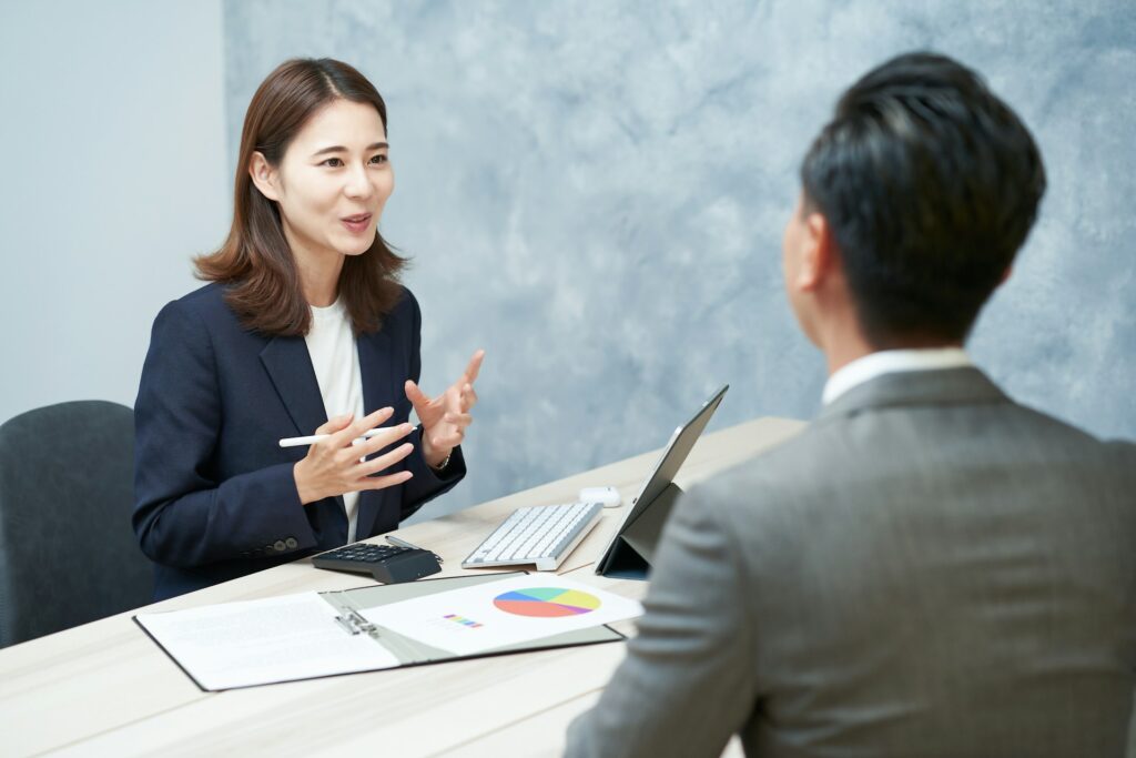 Professional woman discussing business strategies with a client at a table, featuring a laptop, calculator, and colorful pie chart, emphasizing communication in managing business disputes.