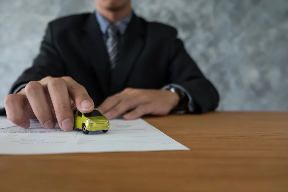 Person in a suit placing a miniature yellow car on legal documents, symbolizing vehicle ownership transfer and probate considerations in Oklahoma.