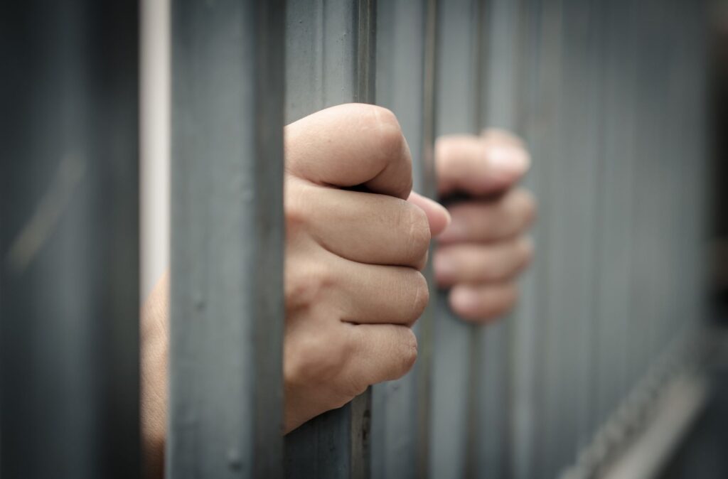 Hands gripping prison bars, symbolizing arrest and the importance of understanding legal rights during criminal defense situations.