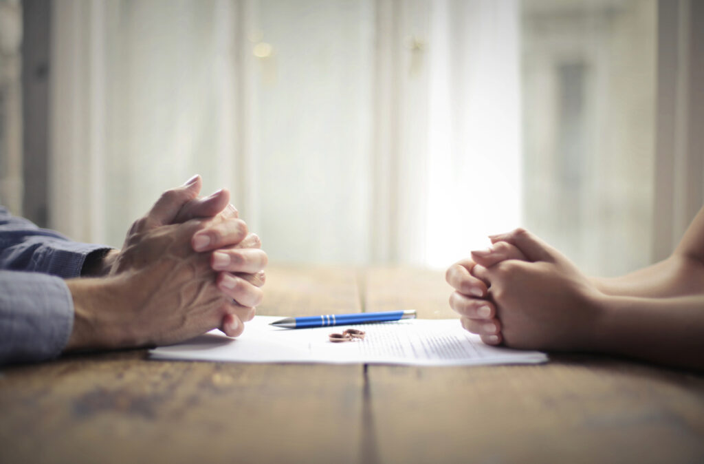 Hands clasped together on a table with documents and a pen, symbolizing discussions about divorce and child custody matters.