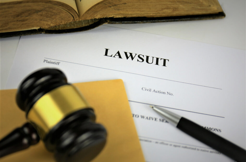 Gavel resting on lawsuit document with "LAWSUIT" header, surrounded by legal paperwork and an open book, symbolizing civil litigation process.