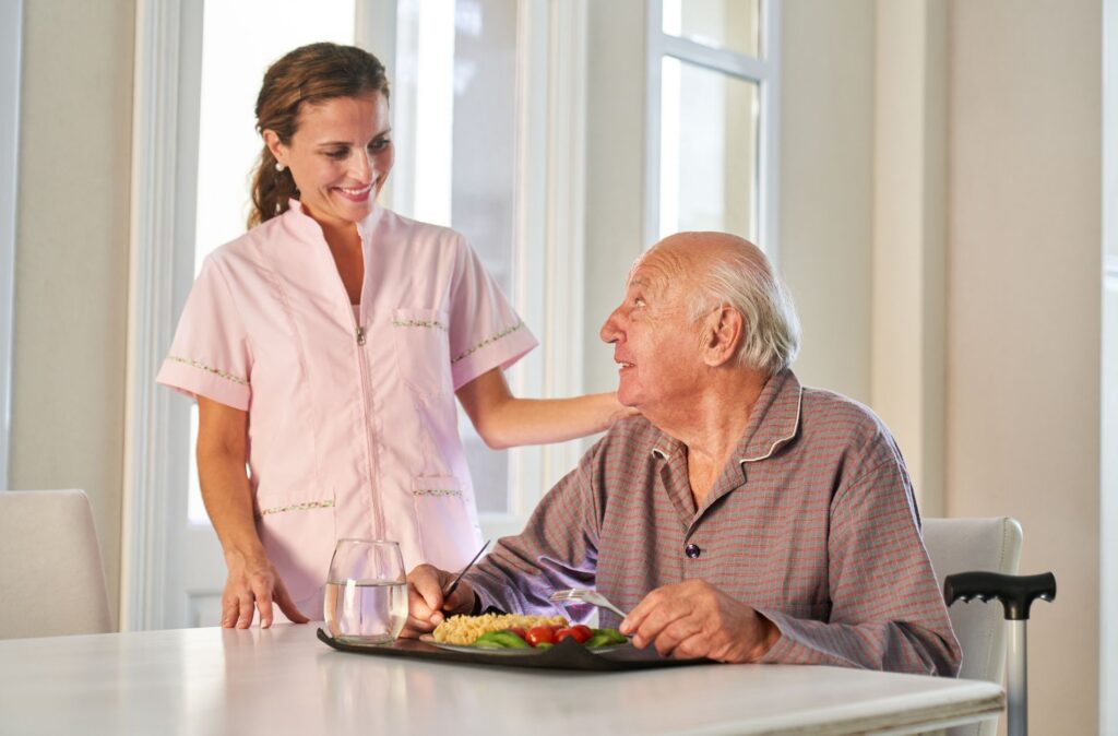 Caregiver assisting elderly man with meal in home setting, highlighting elder care and support for seniors.